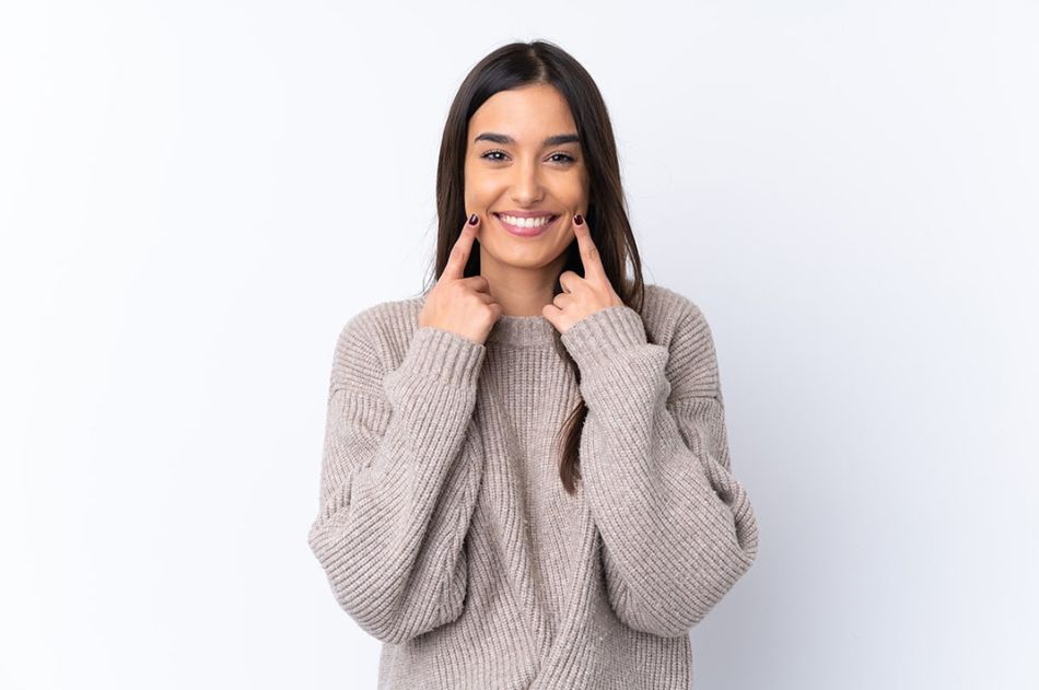 A young woman with long, dark hair using her hands to trace a smile